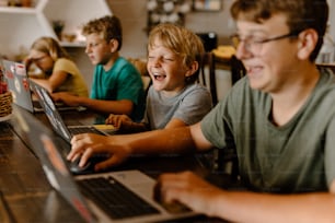 Un grupo de niños sentados en una mesa con computadoras portátiles