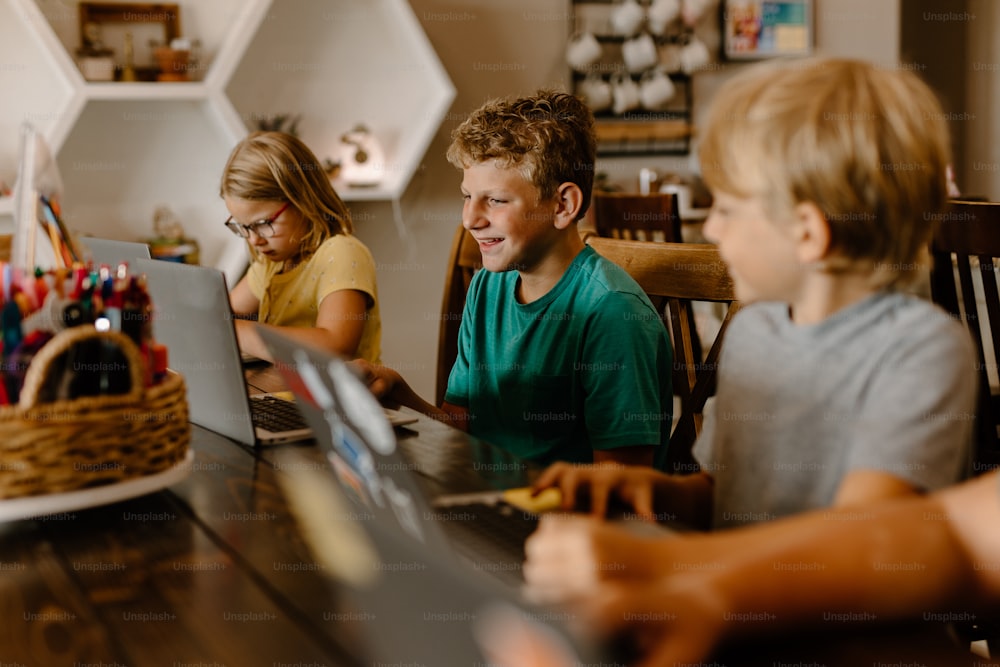 a group of children sitting at a table with laptops