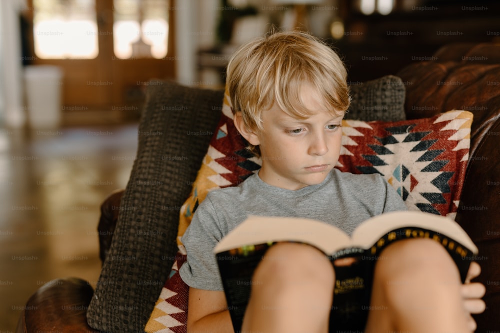 a young boy sitting in a chair reading a book