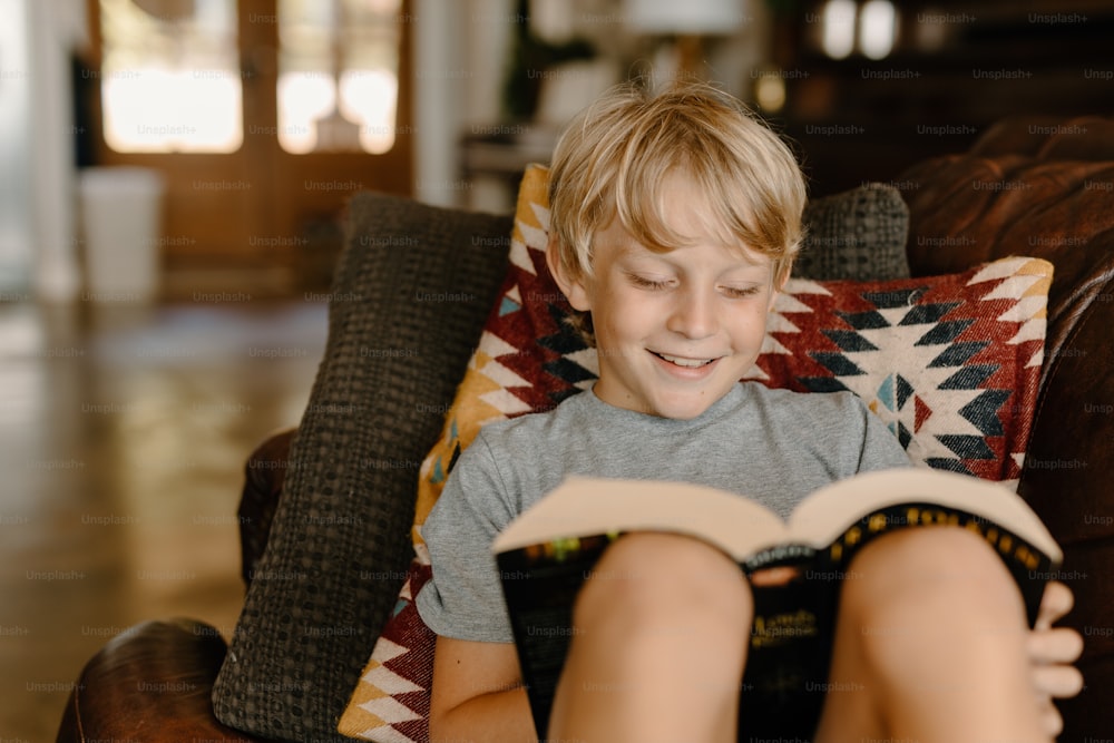 a young boy sitting in a chair reading a book