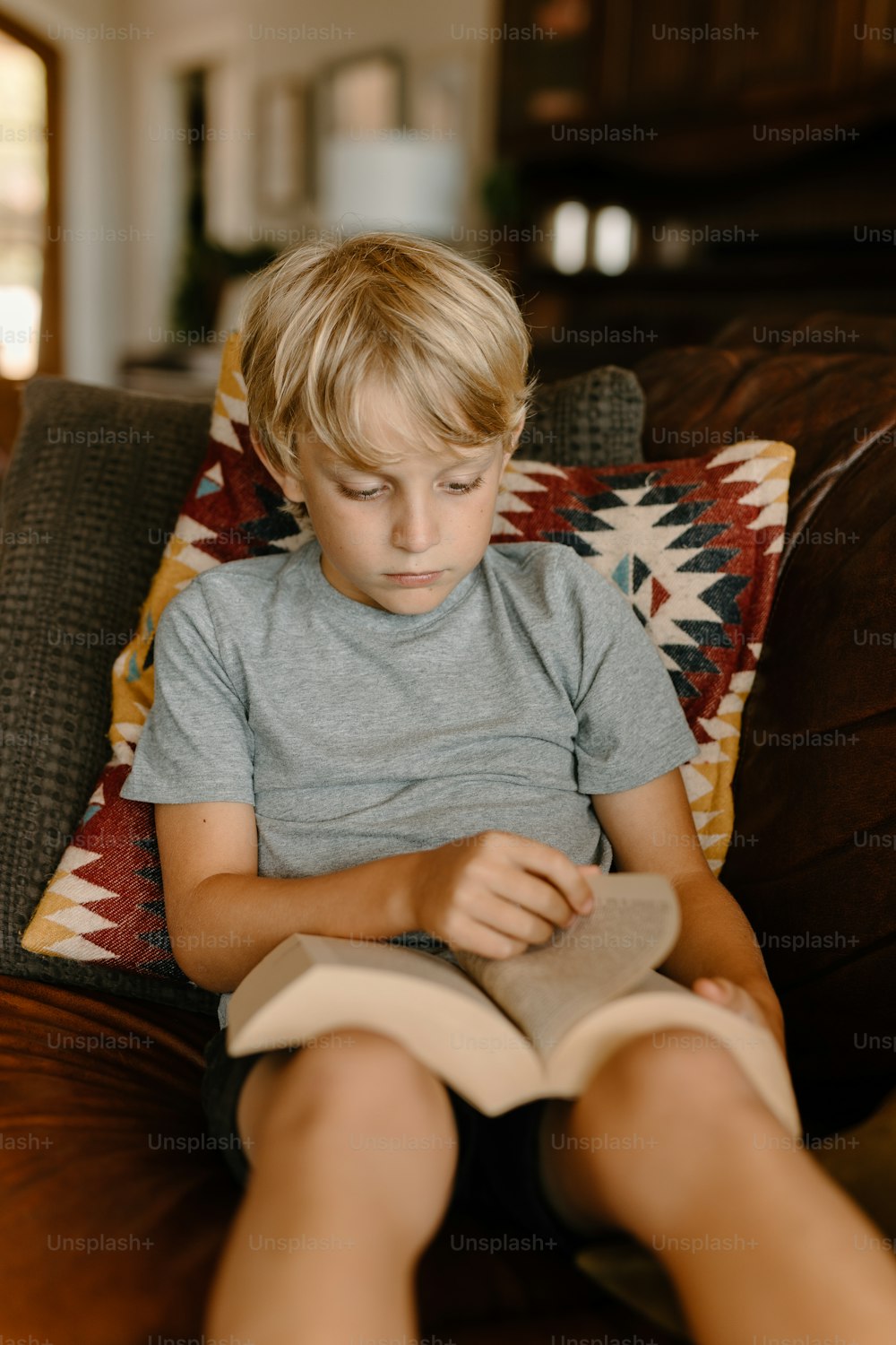 a young boy sitting on a couch reading a book