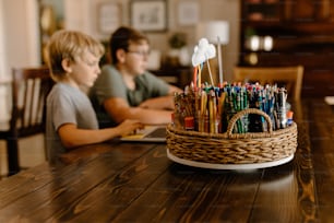 a boy and a boy sitting at a table with a basket full of pens and