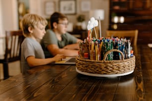 un niño y un niño sentados en una mesa con una canasta llena de bolígrafos y