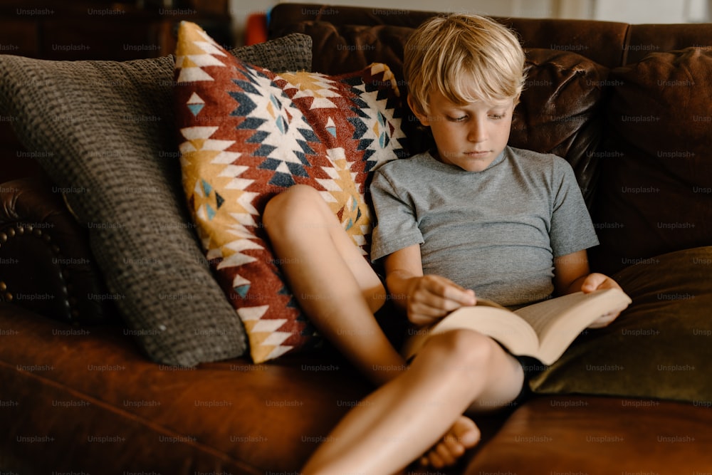 a young boy sitting on a couch reading a book