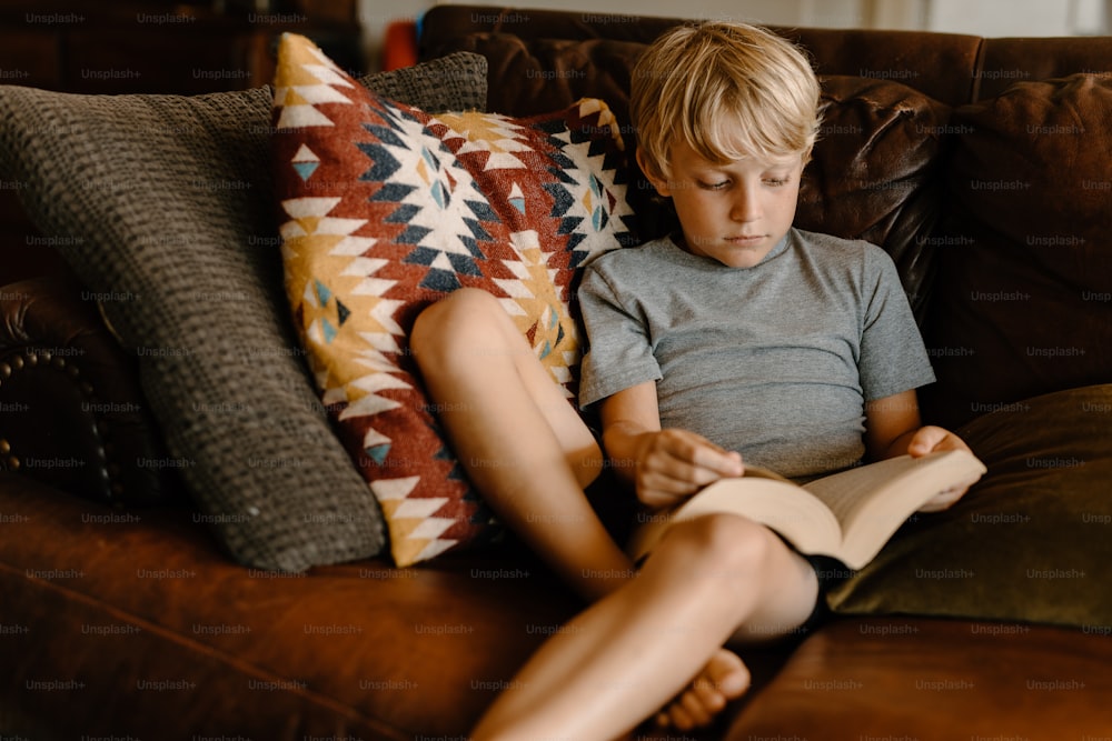 um menino sentado em um sofá lendo um livro