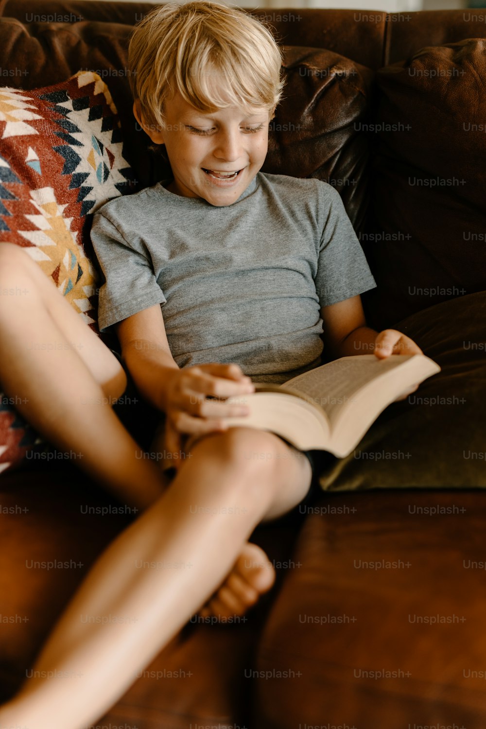 a young boy sitting on a couch reading a book