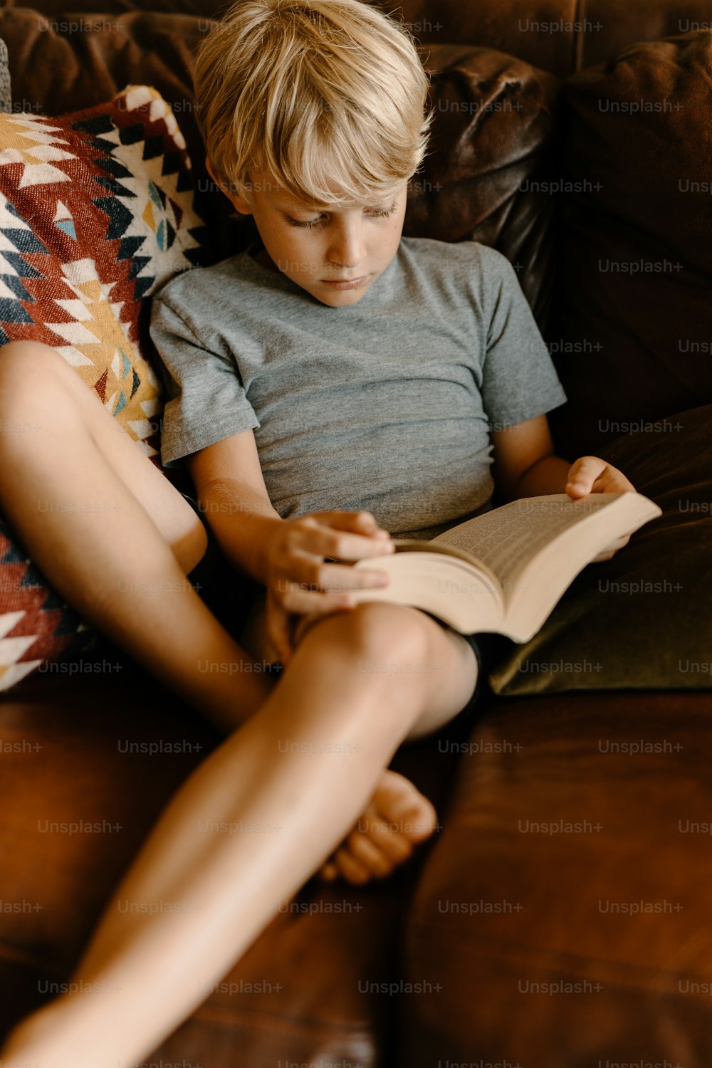 a young boy sitting on a couch reading a book
