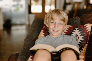 a young boy sitting in a chair holding a book