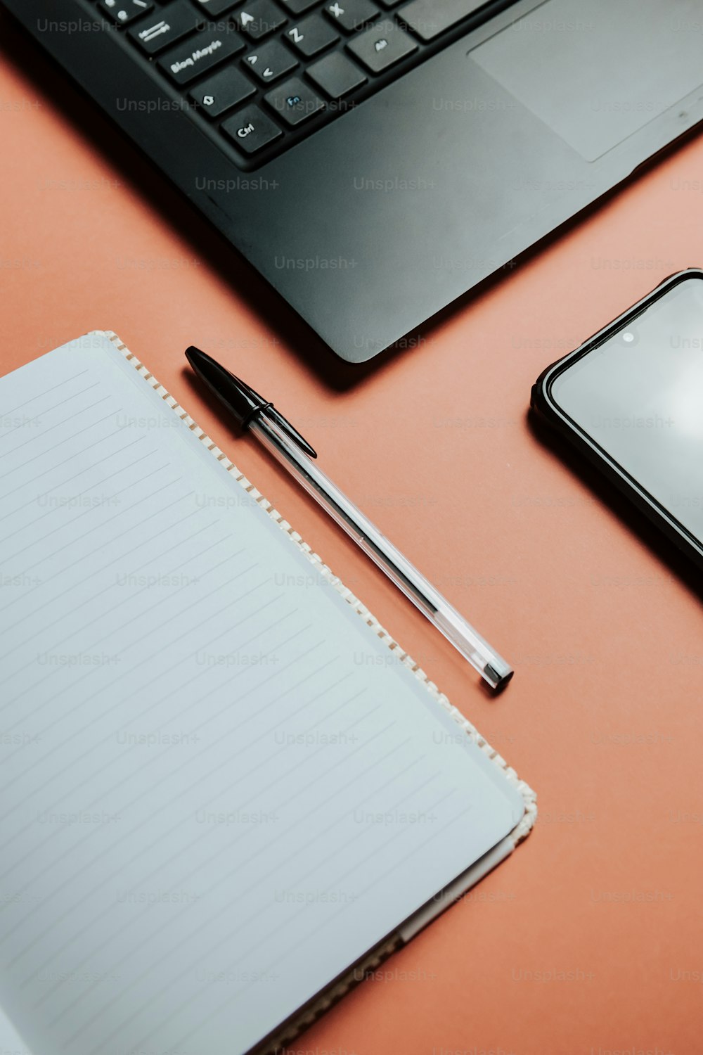 ein Notizbuch, ein Stift, ein Handy und ein Laptop auf einem Schreibtisch