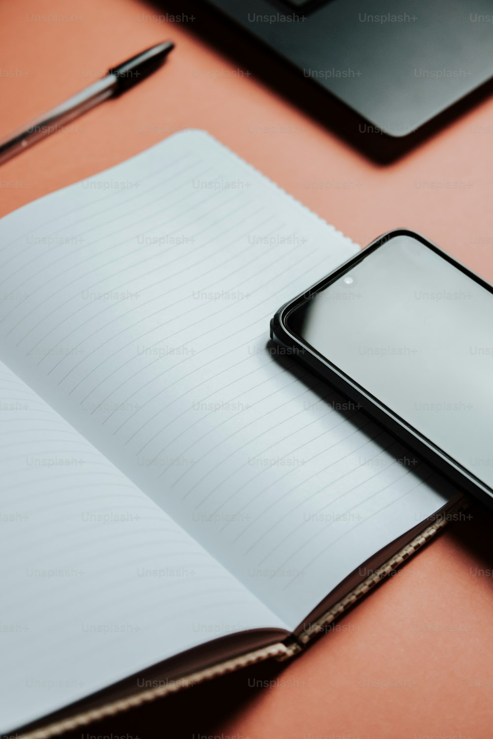 um celular sentado em cima de um caderno ao lado de uma caneta