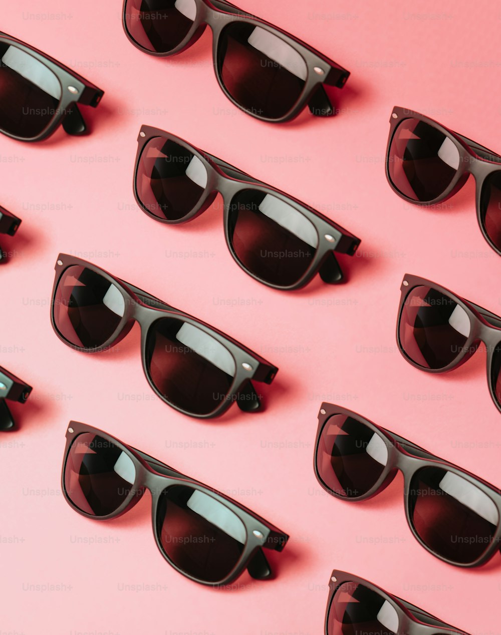 Un montón de gafas de sol sentadas encima de una superficie rosa