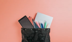 um saco preto cheio de material escolar em cima de um fundo rosa