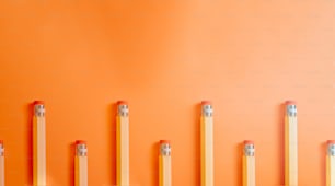 a row of pencils lined up against an orange wall