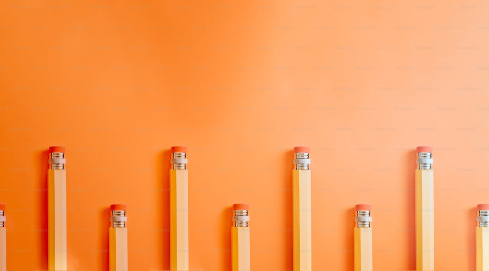 eine Reihe von Bleistiften, die an einer orangefarbenen Wand aufgereiht sind