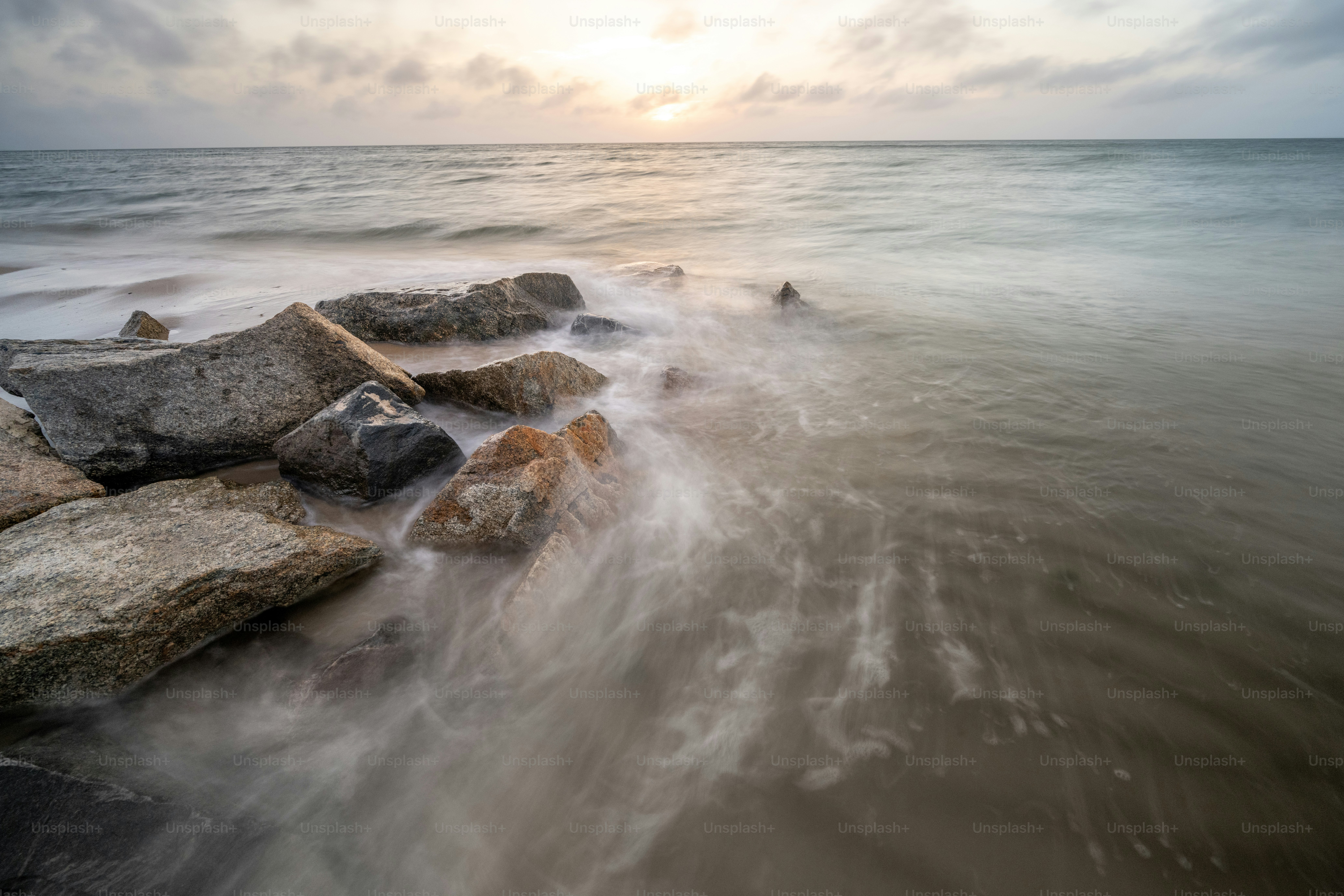 A long exposure photo of the ocean with rocks in the foreground photo ...