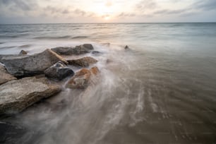 a long exposure photo of the ocean with rocks in the foreground