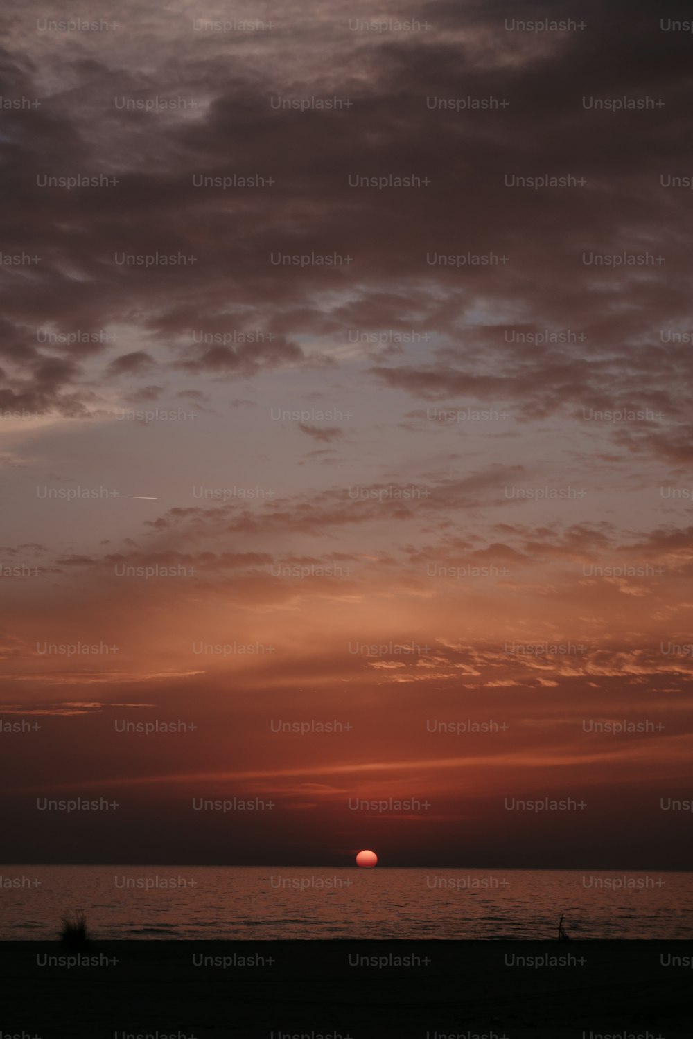 the sun is setting over the ocean on a cloudy day