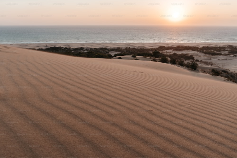 the sun is setting over the ocean and sand dunes