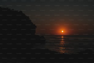 the sun is setting over the ocean as seen from a cliff