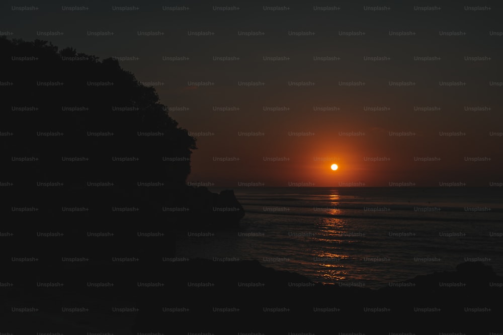 the sun is setting over the ocean as seen from a cliff