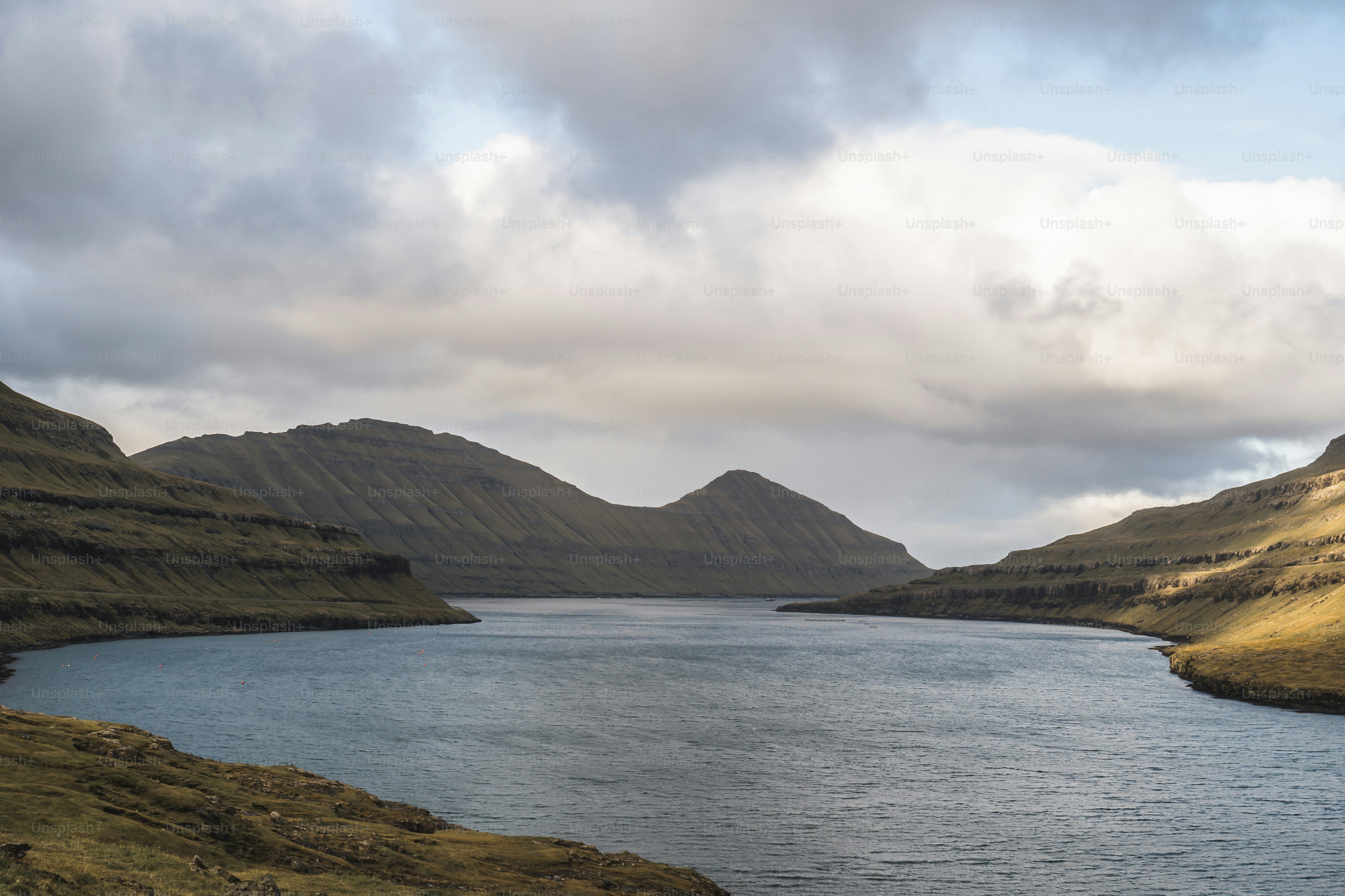 a body of water surrounded by mountains under a cloudy sky