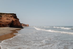 a sandy beach next to a cliff on a clear day