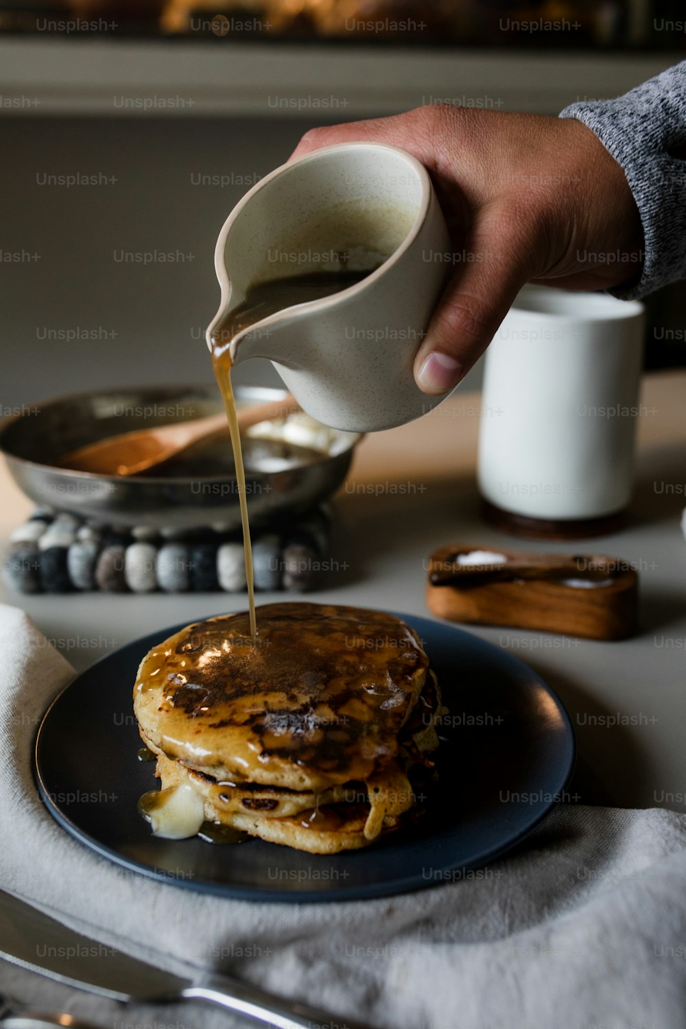 a person pouring syrup on a stack of pancakes