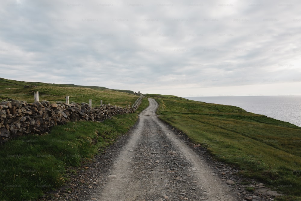 a gravel road with a stone wall next to the ocean