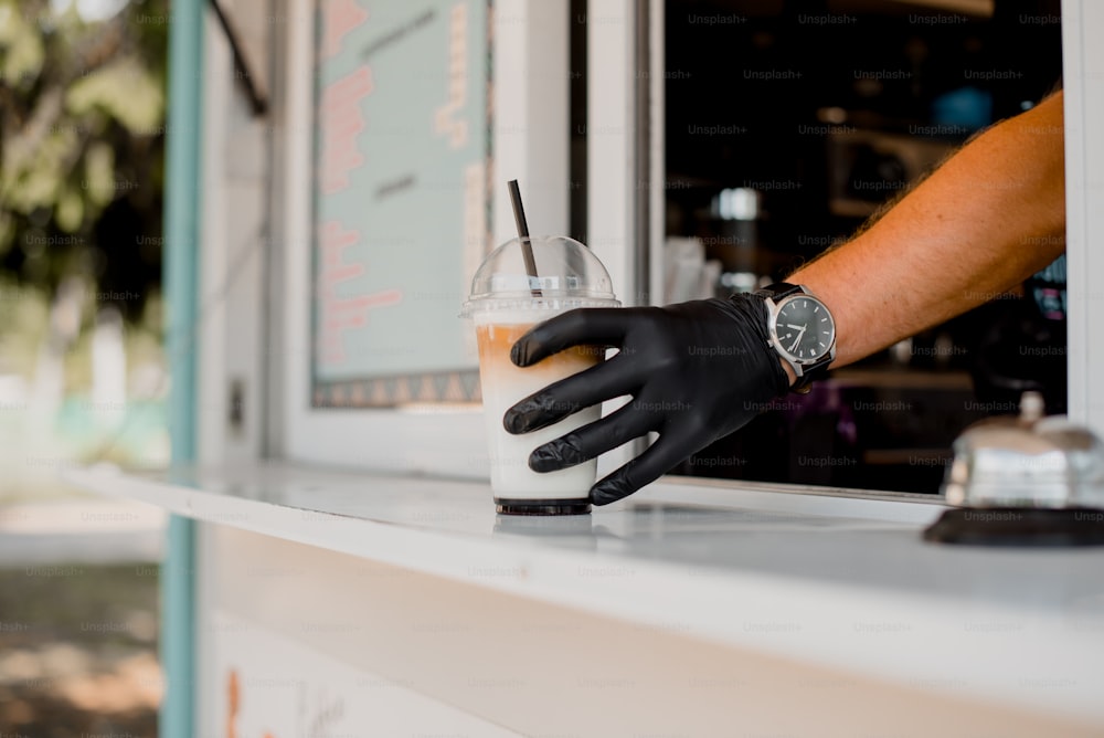 a person wearing black gloves is holding a drink