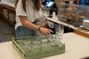 a woman in a white shirt is putting glasses in a green tray
