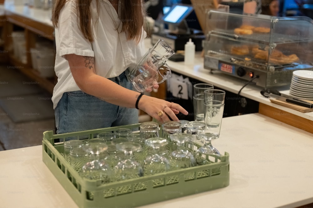 a woman in a white shirt is putting glasses in a green tray