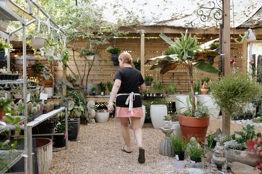 a woman walking through a garden shop filled with potted plants