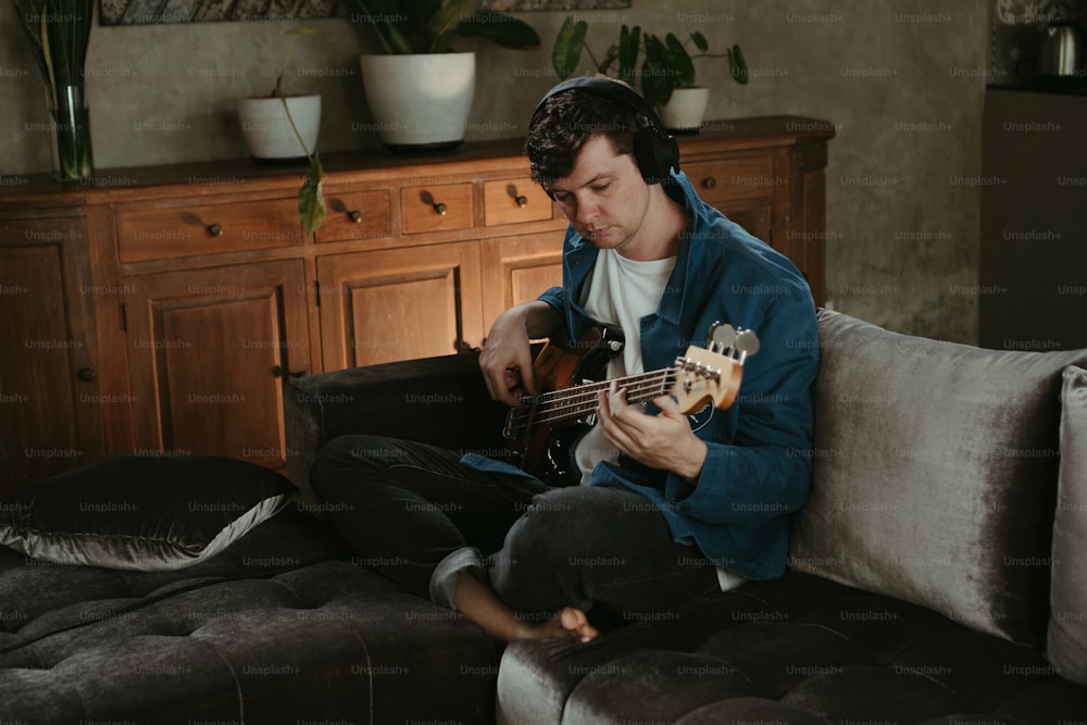 um homem sentado em um sofá tocando uma guitarra