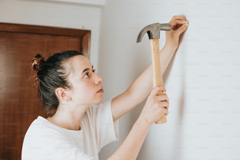 a woman holding a hammer up to a wall