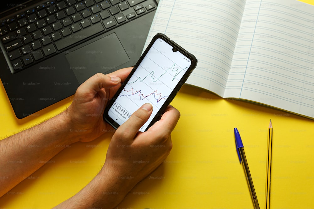 Una persona sosteniendo un teléfono celular junto a una computadora portátil