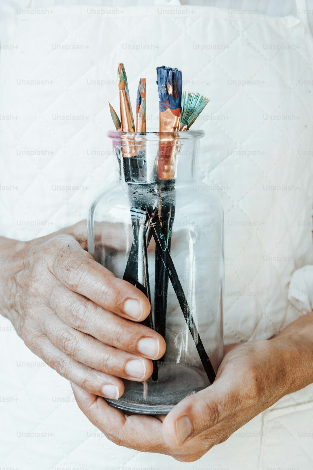 uma pessoa segurando um frasco cheio de canetas e lápis