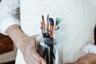 a person holding a jar filled with paint brushes