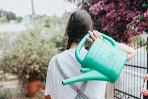 a woman is holding a green watering can