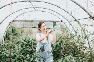 a woman in overalls holding a bird in a greenhouse