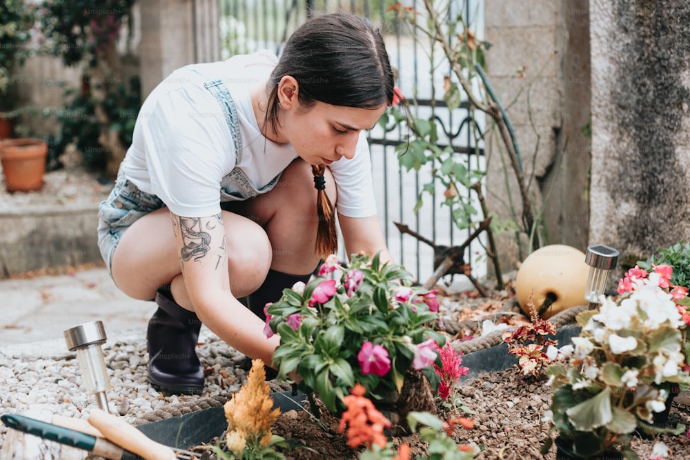 a woman kneeling down to plant flowers in a garden