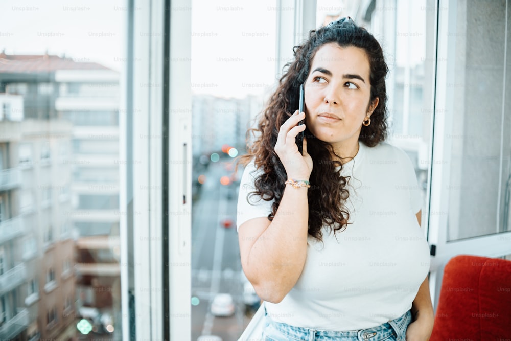 Una mujer hablando por teléfono celular frente a una ventana