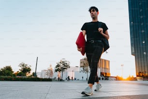 Un uomo che cammina lungo un marciapiede portando una borsa rossa