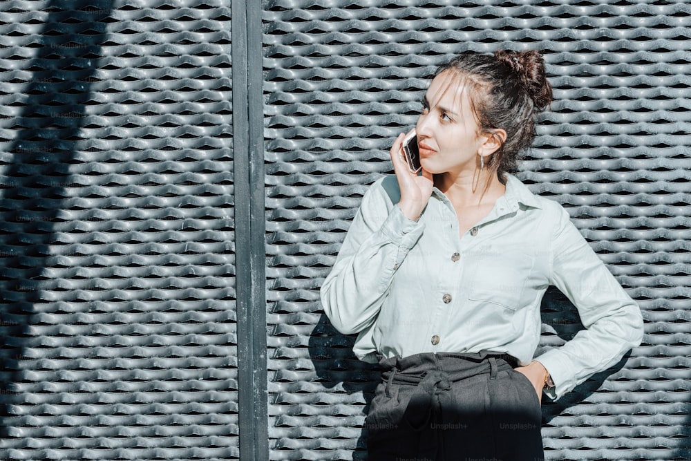 a woman standing in front of a wall talking on a cell phone