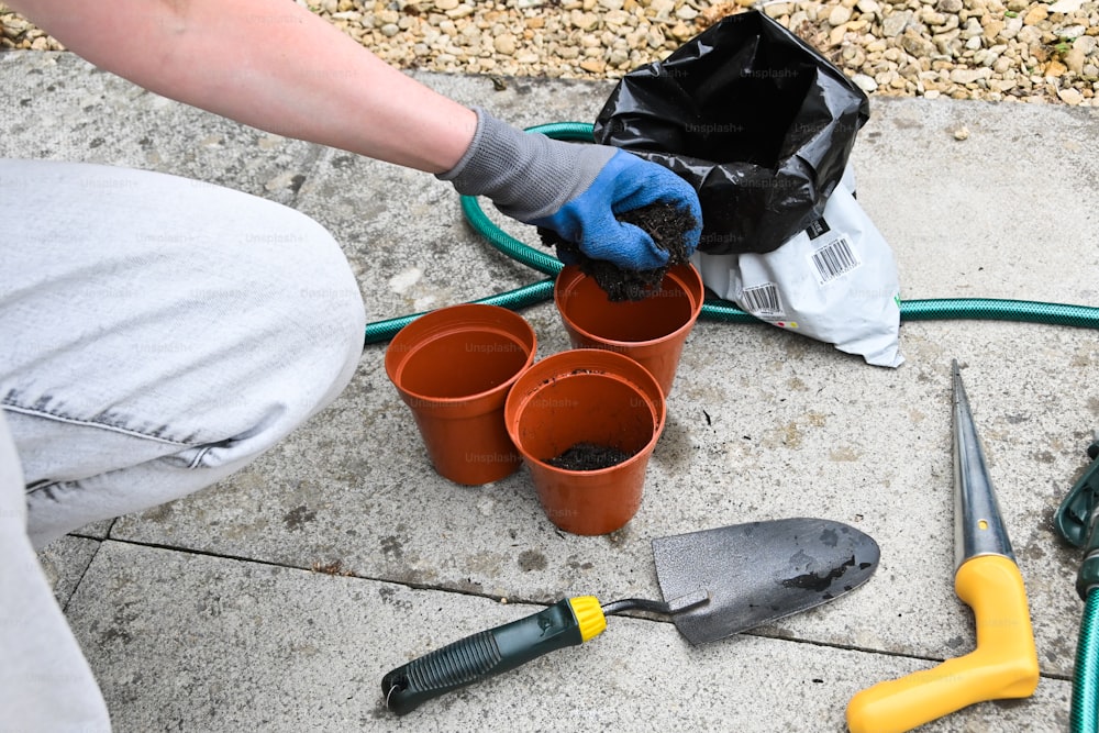 uma pessoa com luvas e ferramentas de jardinagem no chão