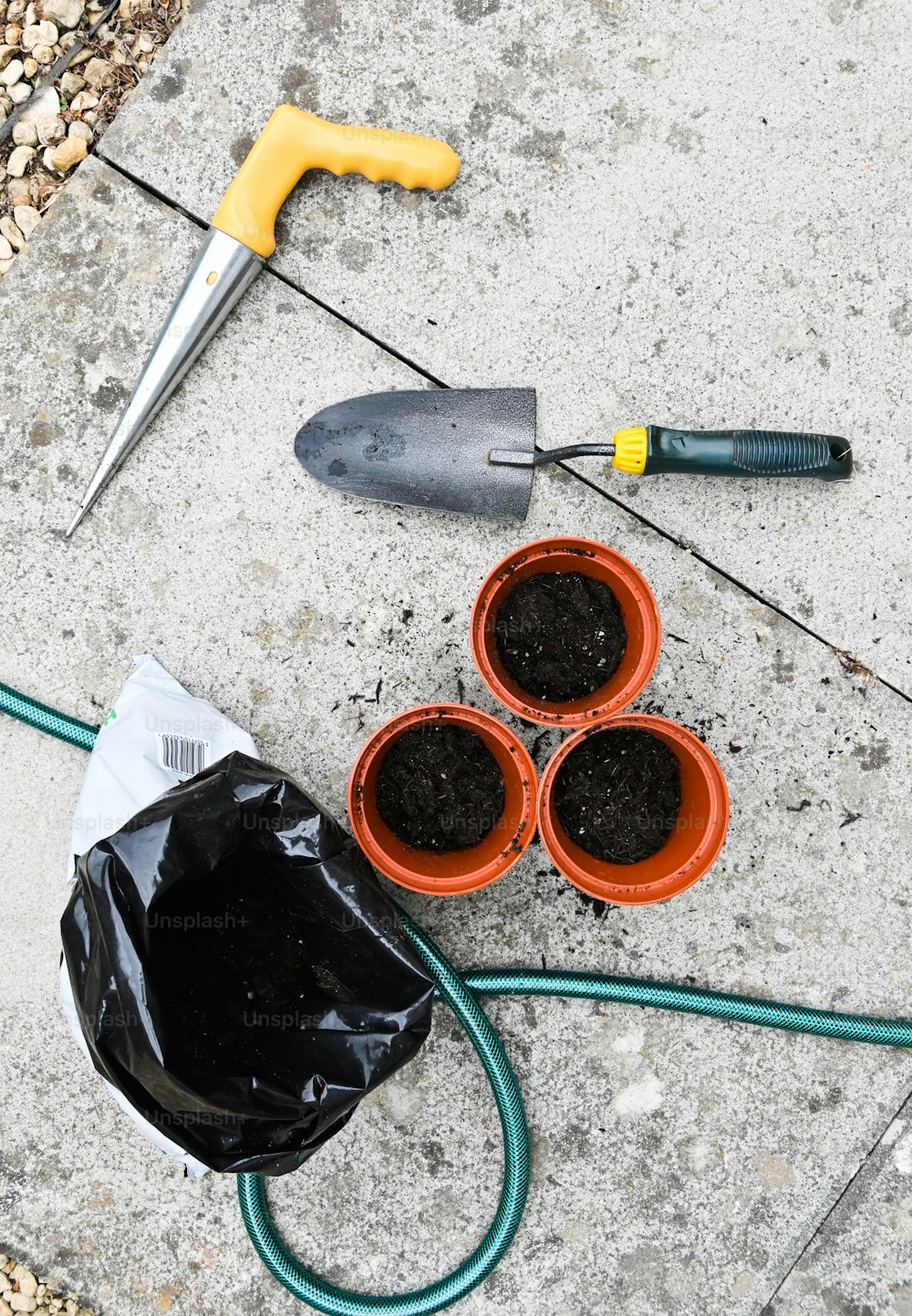 a couple of pots of dirt next to a garden hose