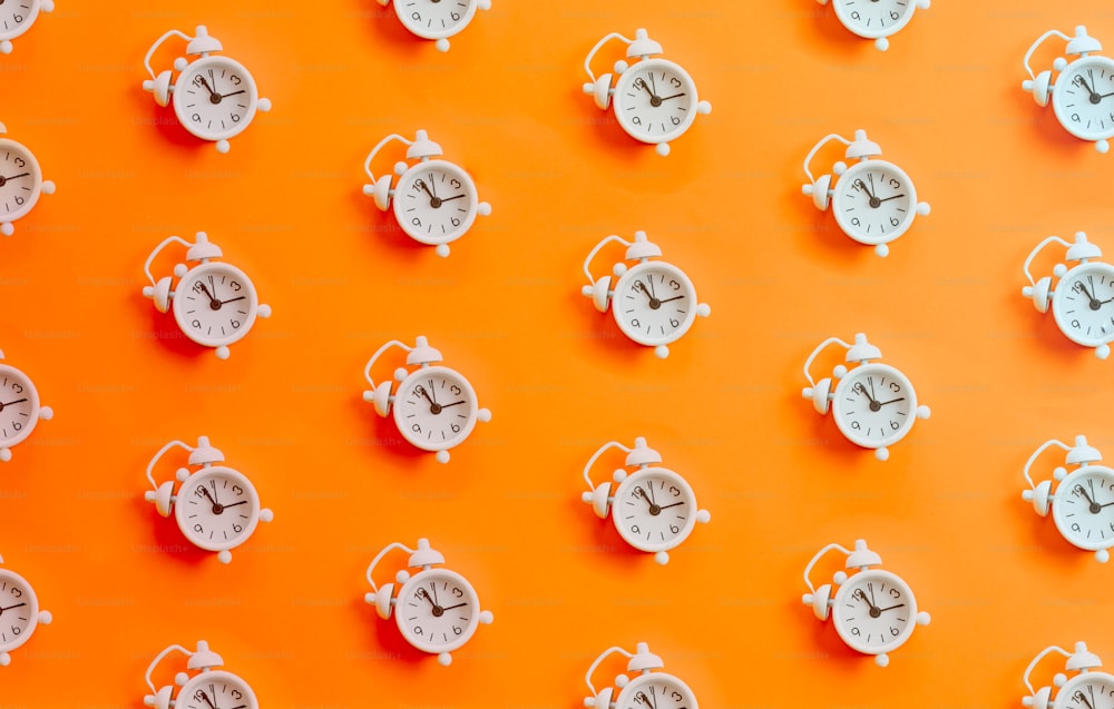 Eine Gruppe weißer Uhren an einer orangefarbenen Wand