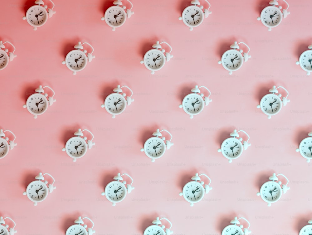 a pink wall with many clocks on it