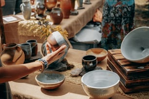 a woman is holding a cup over a table full of pottery