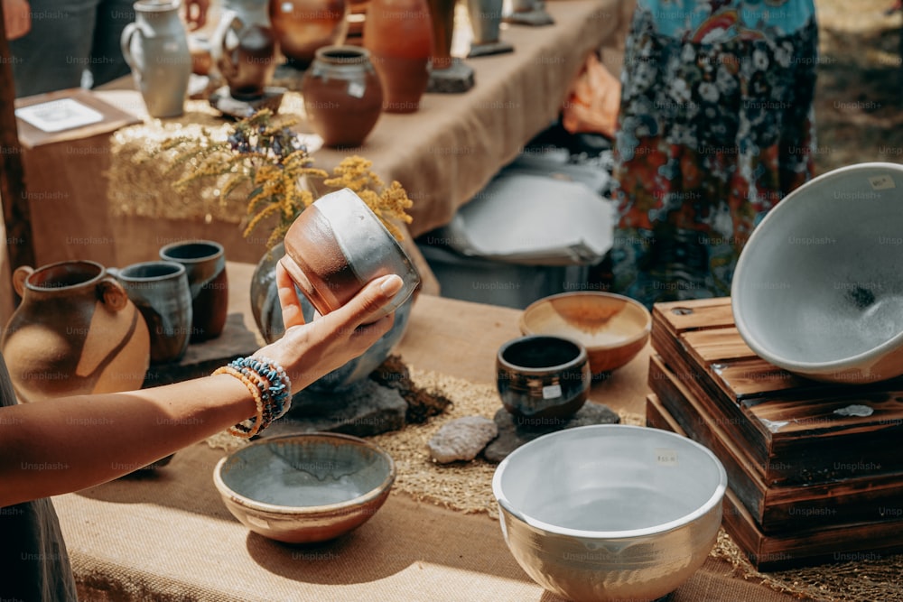 a woman is holding a cup over a table full of pottery