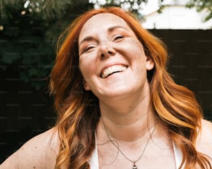 a woman with red hair smiling and wearing a necklace